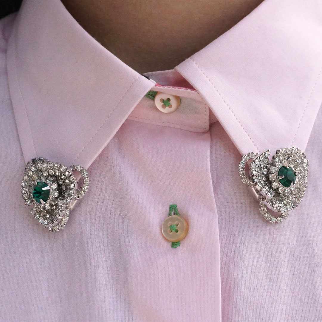 How to wear vintage: Hattie Carnegie emerald and diamante dress clips are shown separated on the collar of a pink shirt