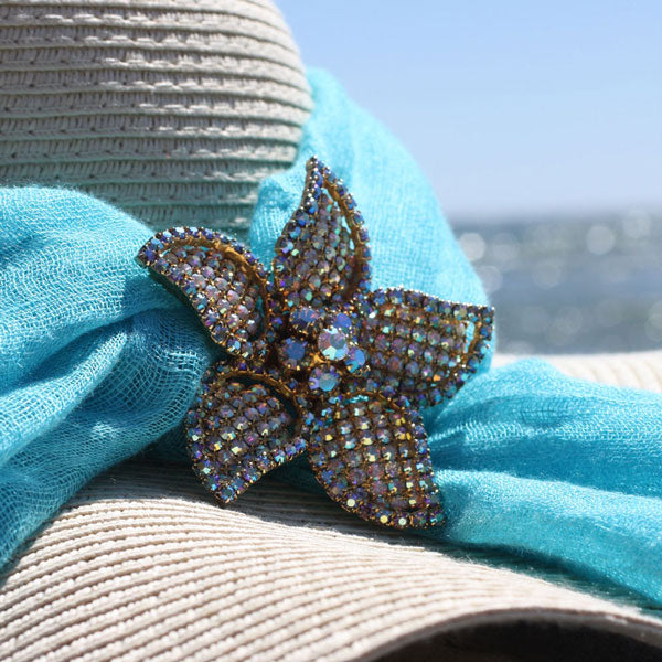 Alice Caviness aurora borealis starfish brooch pinned on straw beach hat with water sparkling in the distance